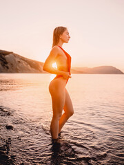 Pretty young woman in red bikini at sea beach with sunset