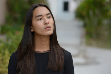Face of young Asian man with long hair thinking at the park - Powered by Adobe
