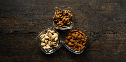 Almond, pistachio and walnut in a small plates which standing on a vintage wooden table. Nuts is a healthy vegetarian protein and nutritious food.