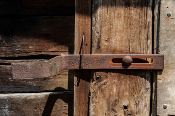 Old rusty metal deadbolt on the barn door, against the background of a wooden wall made of railway sleepers.