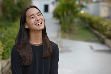Happy young Asian man with long hair smiling at the park