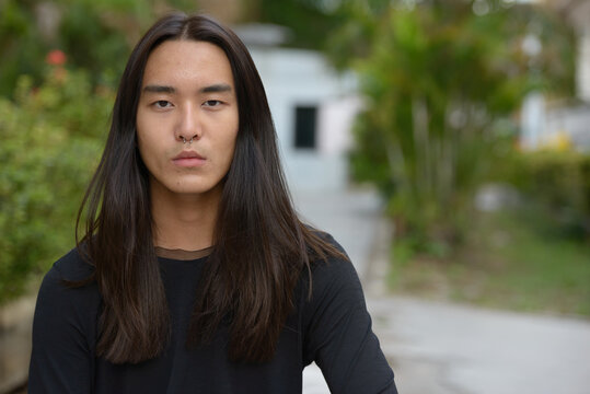 Face of young Asian man with long hair at the park
