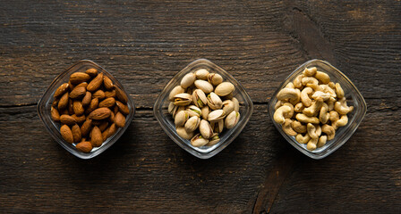 Almond, pistachio and cashew in a small plates which standing on a vintage wooden table. Nuts is a healthy vegetarian protein and nutritious food.