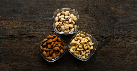 Almond, pistachio and cashew in a small plates which standing on a vintage wooden table. Nuts is a healthy vegetarian protein and nutritious food.