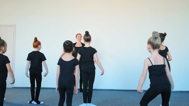 former ballerina and small children jump practicing dance moves at ballet class for beginners in large studio slow motion