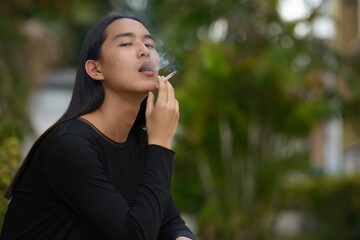 Young Asian man with long hair smoking at the park