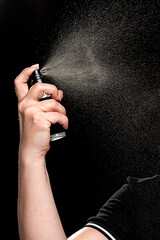 Female hand sprays a skin care spray in the air. Close-up, black background.