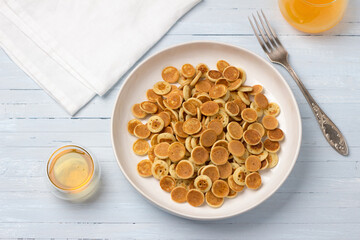 Plate of Mini Pancakes cereals with honey and fresh orange juice on a light blue background. trendy food. homemade breakfast. top view