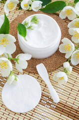 White facial mask (face cream, hair mask, body butter, facial cleanser) in the small white jar, cotton pads and jasmine flowers. Natural skin and hair treatment concept. Top view, copy space.
