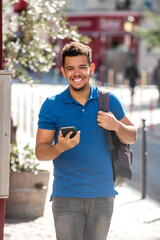 smiling young african american man walking with mobile phone and bag in city