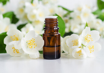 Small glass bottle with essential jasmine oil (tincture, infusion, perfume) on the white background. Jasmine flowers close up. Aromatherapy, spa and herbal medicine ingredients. Copy space.