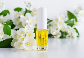Obraz na płótnie Canvas Small bottle with cosmetic oil (massage cuticle oil, tincture, infusion, extract) and jasmine flowers close up. Aromatherapy, natural manicure, homemade spa and herbal medicine concept. Copy space.