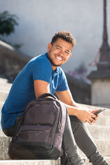 Obraz premium smiling young african american man sitting on steps outside with mobile phone