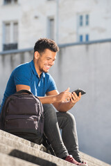 happy young african american mixed race man sitting on steps looking at mobile phone