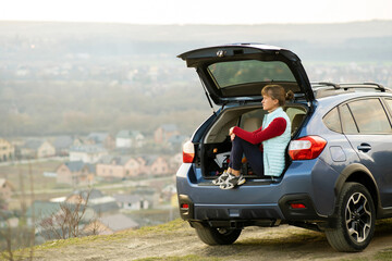 Young woman driver sitting alone in her car enjoying view of nature landscape.