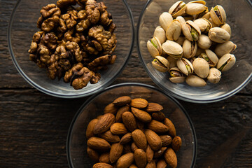 Almond, pistachio and walnut in a small plates which standing on a vintage wooden table. Nuts is a healthy vegetarian protein and nutritious food.