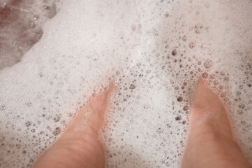Woman bare feet in soap water at home in bathroom.