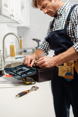 Selective focus of plumber holding handle of faucet near open toolbox in kitchen