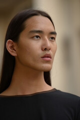 Face of young Asian man with long hair thinking in the city