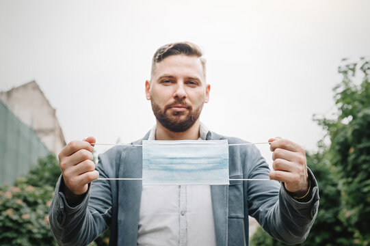 Presentable man holds a disposable mask in front of him in the street. Selective focus.