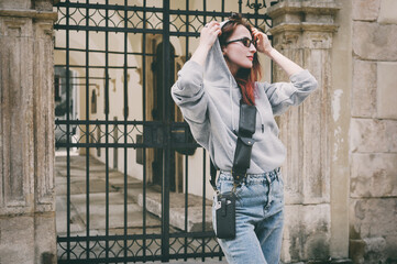 Brunette girl in glasses and a gray sweatshirt on the street near a black gate. On her shoulder Leather Utility Belt Pouch, Utility Belt, Cell Phone Crossbody Purse. Selective focus.