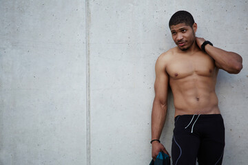 Portrait of handsome fit man with defined, muscular chest and abdominal standing at copy space wall background, shirtless young man taking break after workout, sexy fashion man posing outdoors