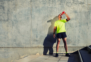 Full length portrait of sweaty man runner refreshing with energy drink water after jogging against cement wall background with copy space area for your text message or content,sportsman having a rest