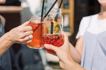 Three young women holding glasses of fresh cocktails and making celebratory toast at summer party.