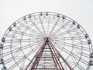 Photo From the bottom up of a tall modern Ferris wheel with enclosed booths against a cloudy sky.
