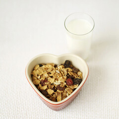 Muesli in heart bowl with a glass of milk