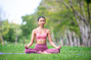 Asian model poses yoga in a park on a natural green background, health care concept, beautiful body structure, fit body
