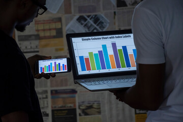 two young african business men viewing graph information on a mobile phone and laptop computer, contemplating ideas, planning