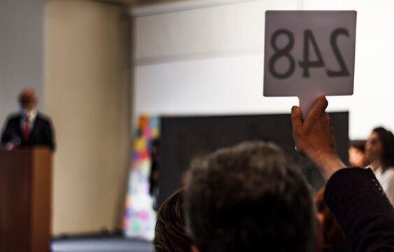 Ongoing auction session. a buyer raises his number sign to buy a painting