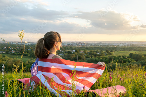 Happy young woman posing with USA national flag standing outdoors at sunset. Positive girl celebrating United States independence day. International day of democracy concept.