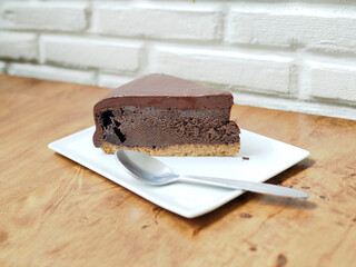 Cutting piece of rich chocolate tart cake with spoon served in white plate on wooden table. Selective focus.