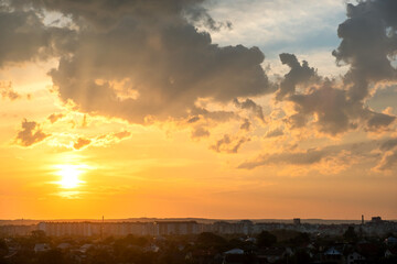 Dramatic sunset over rural area with puffy clouds lit by orange setting sun and blue sky.