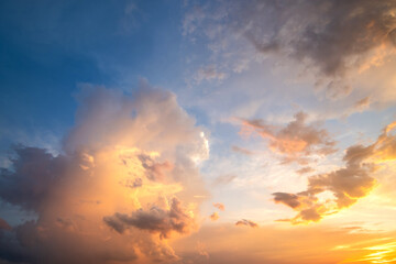 Dramatic cloudy sunset landscape with puffy clouds lit by orange setting sun and blue sky.