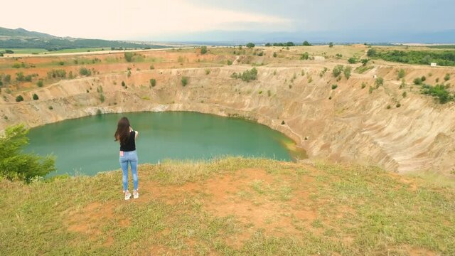 Lonely woman taking photos of open mine pit filled with blue water in Tsar Asen village, Bulgaria