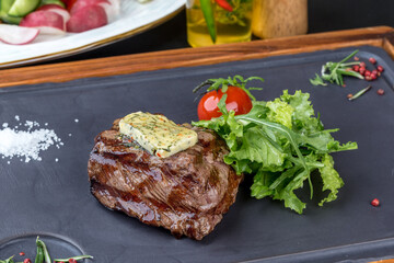Steak mignon with fresh herbs on a black slate blackboard