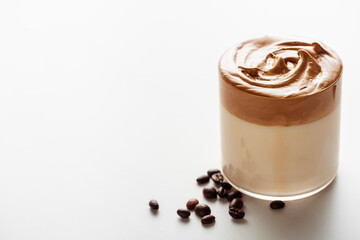 delicious Dalgona coffee in glass near coffee beans on white background