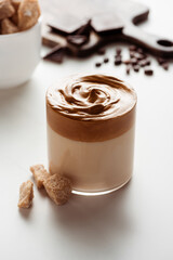 selective focus of delicious Dalgona coffee in glass near brown sugar on white background