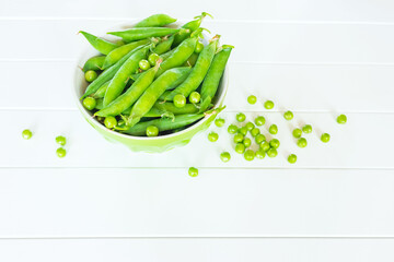 sweet green pea pods in a bowl on a white background close-up. pods of green peas and peas on the table close-up.