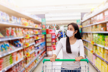 Asian woman wearing protective face mask  push shopping cart in supermarket department store. Girl looking grocery to buy something. During coronavirus crisis or covid19 outbreak. new normal concept