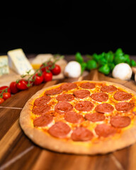 Pepperoni Pizza on a wooden pizza board with lots of ingredients and around. Concept of freshly homemade pizza with a lot of pepperoni salami on the top with free space for your text/decoration. 