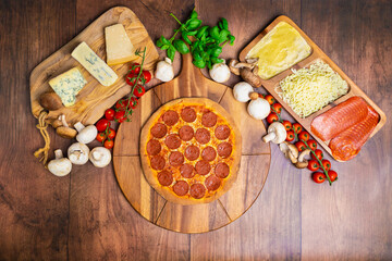Pepperoni Pizza on a wooden pizza board with lots of ingredients and around. Concept of freshly homemade pizza with a lot of pepperoni salami on the top with free space for your text/decoration. 