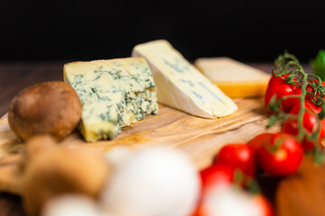 Blue cheese, goats cheese, and parmesan cheese on a wooden board along with tomato, basil, mushrooms. Concept of pizza ingredients with free space for your decoration/text.