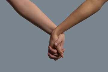 Close-up of light-skinned and dark-skinned people holding hands