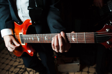 Obraz premium The musician plays the electric guitar on stage. Guitar neck close-up on a concert of rock music in the hands of a musician. Fingers on fretboard