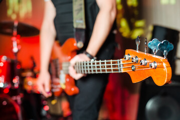 Naklejka premium The musician plays the electric bass guitar on stage. Guitar neck close-up on a concert of rock music in the hands of a musician. 