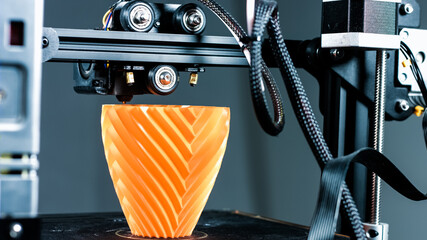3D Printer printing a vase for home decoration with orange plastic Filament.